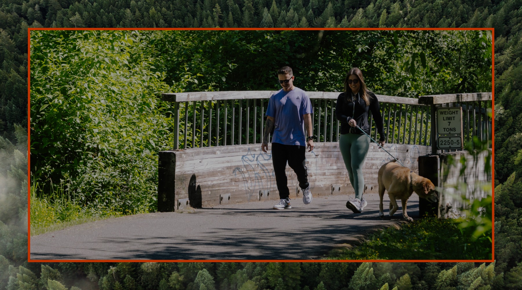 Two people walking dog on a trail in the woods
